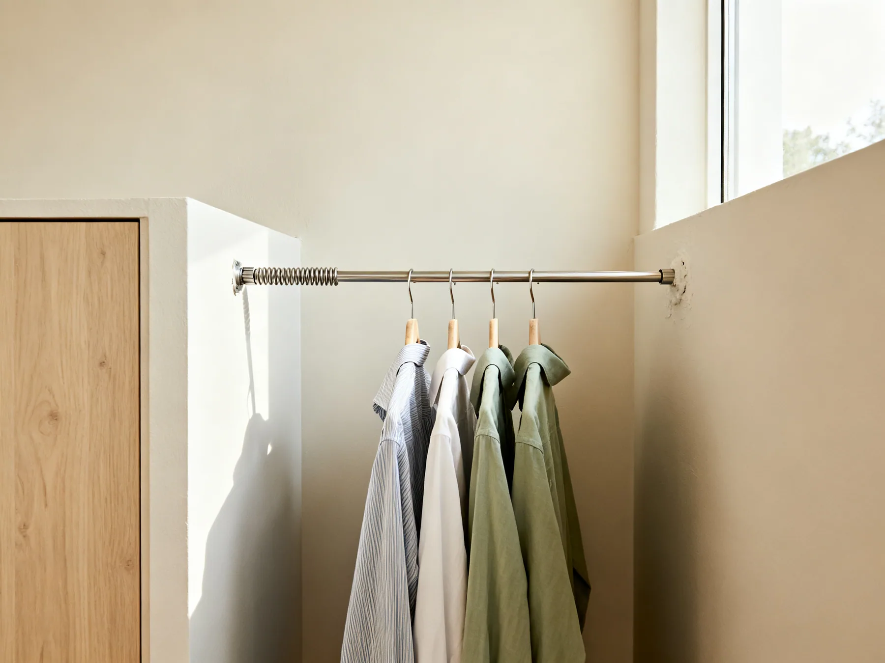 A tension rod, no fixings at all A spring-loaded tension rod wedged between the side walls of an alcove carrying hanging shirts, with no brackets or fixings anywhere