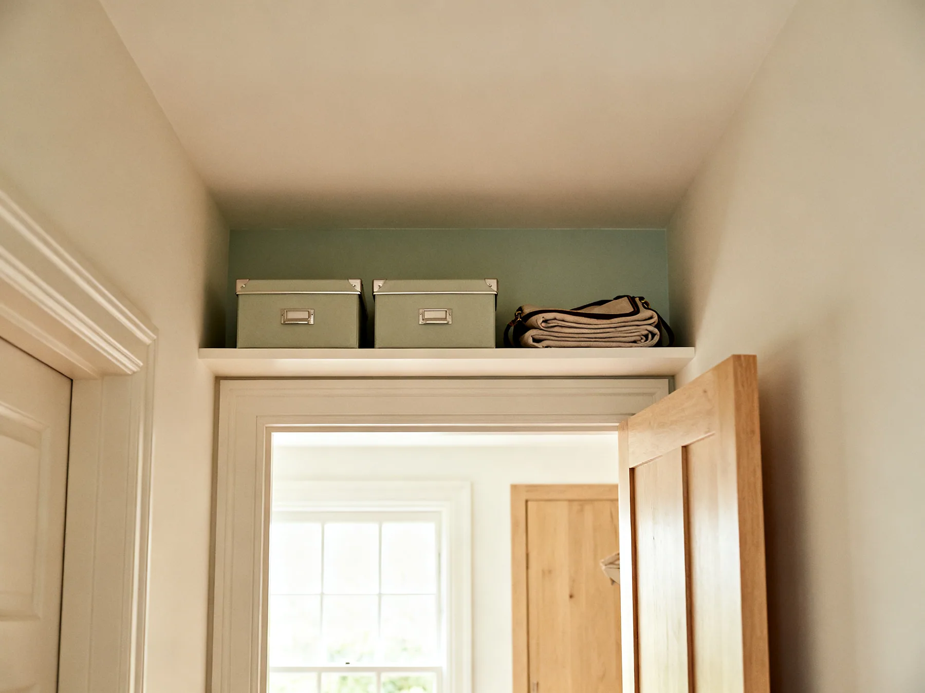 Above the door, where nobody looks A hallway with a shelf fitted above a doorway holding two lidded boxes and a folded bag