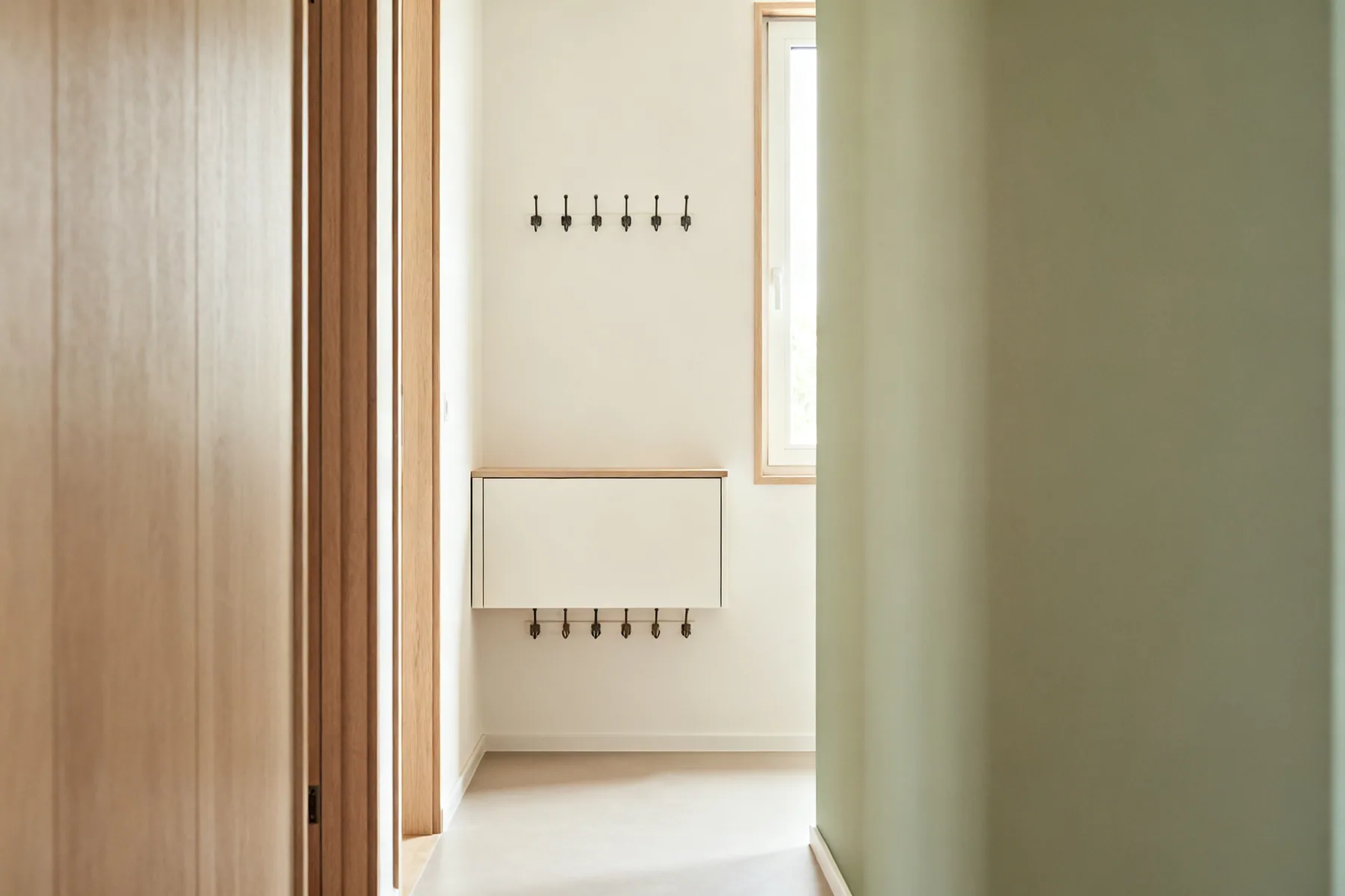 A hallway is a corridor first and storage second A narrow hallway with a slim wall-hung unit about 250mm deep, hooks at two heights above it, and a completely clear floor