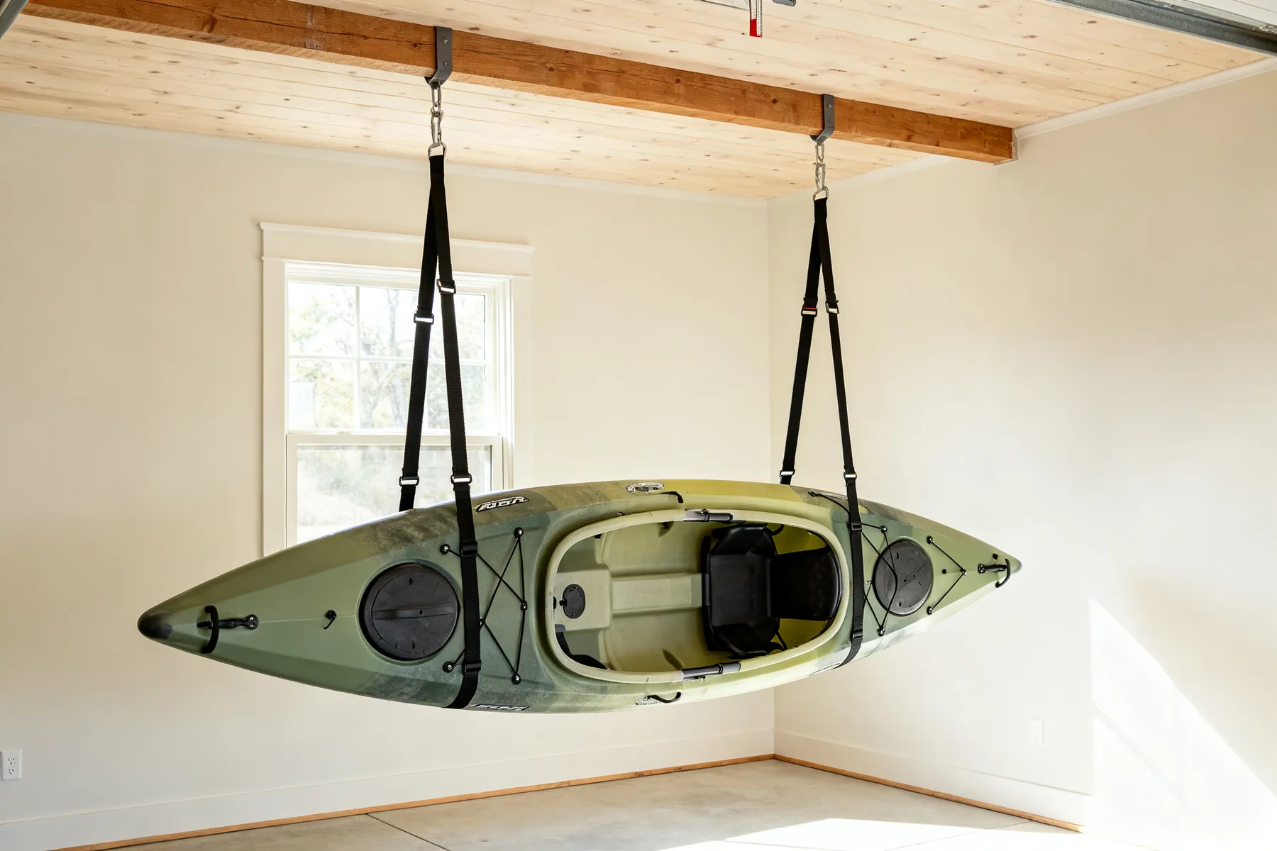 Wide slings, hull upward A kayak hanging upside down in two wide webbing slings from garage ceiling joists, clear of the floor