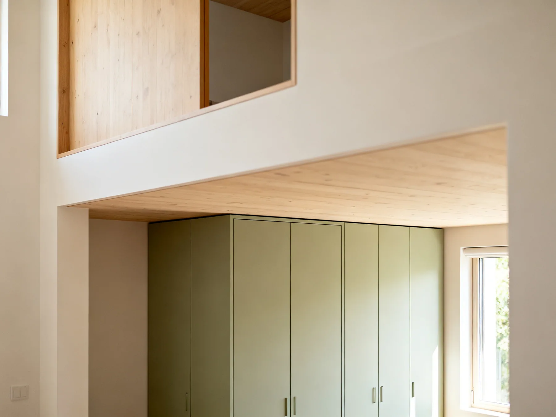Low headroom is storage, not living space The area beneath a mezzanine platform in a loft apartment fitted with full-height cupboards, using the low headroom for storage