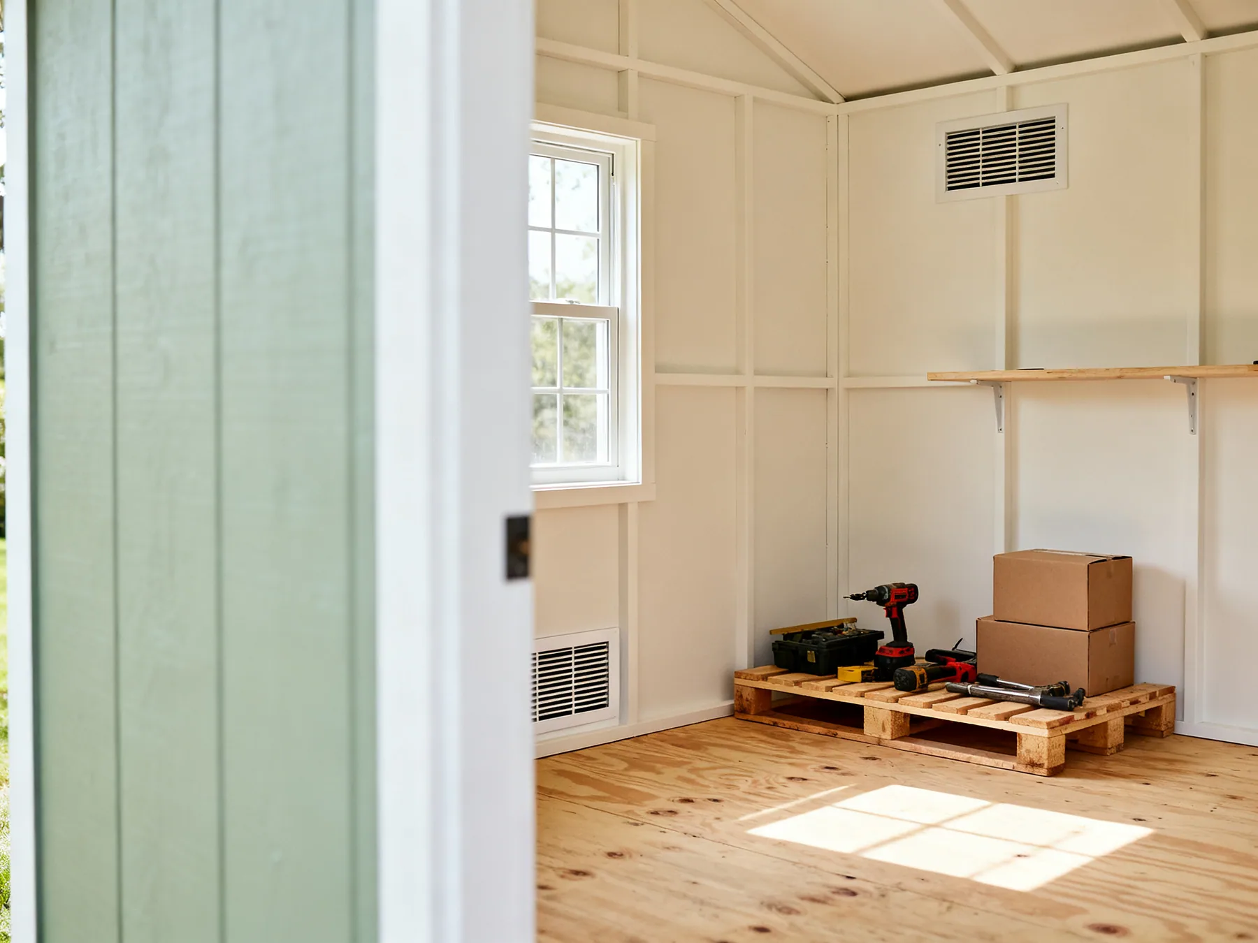 Low vent, high vent, nothing on the floor A shed corner with a low vent near the floor and a high vent on the opposite wall, and tools and boxes raised off the floor on a timber pallet and a wall shelf
