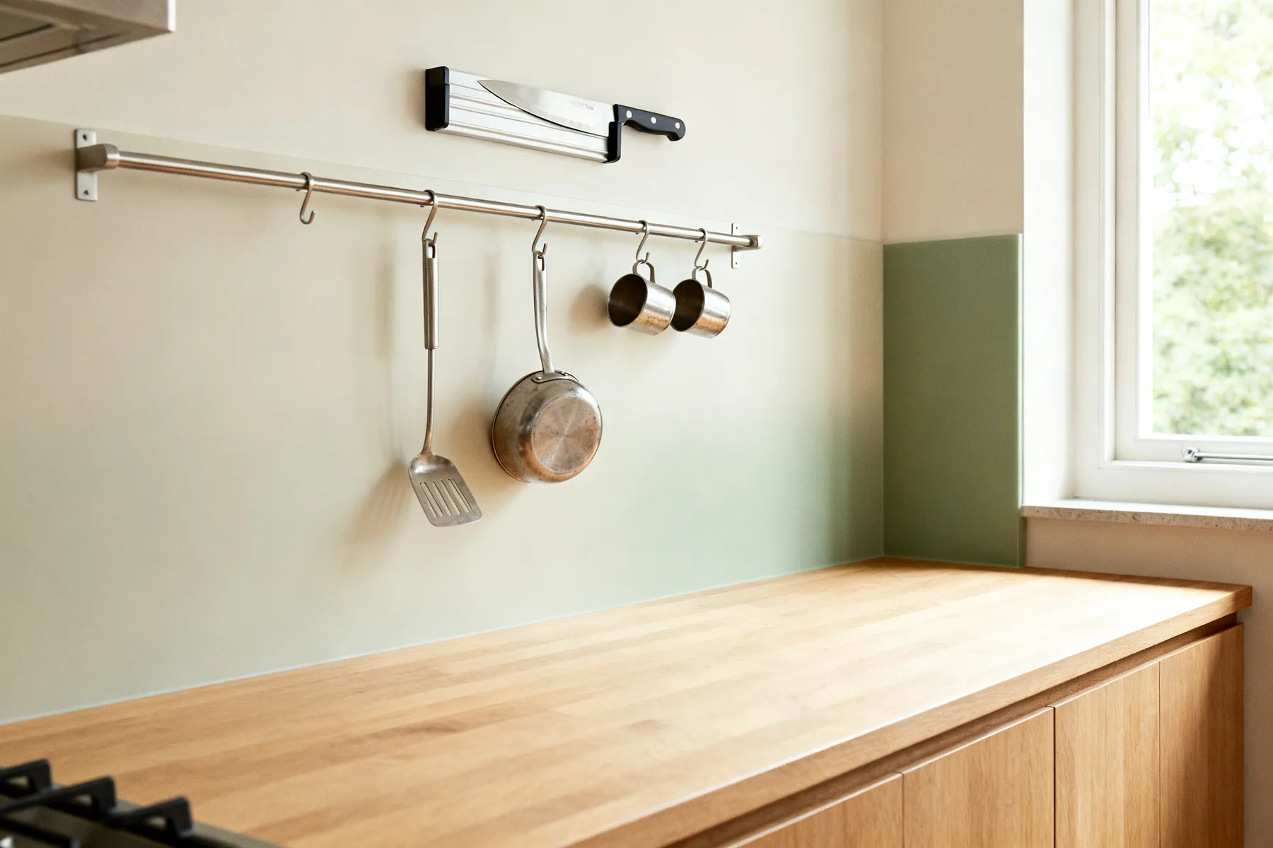 Get the daily tools off the counter and onto the wall A kitchen splashback with a slim steel rail carrying hanging utensils and small hooked pots, and a magnetic knife strip above, with clear worktop beneath