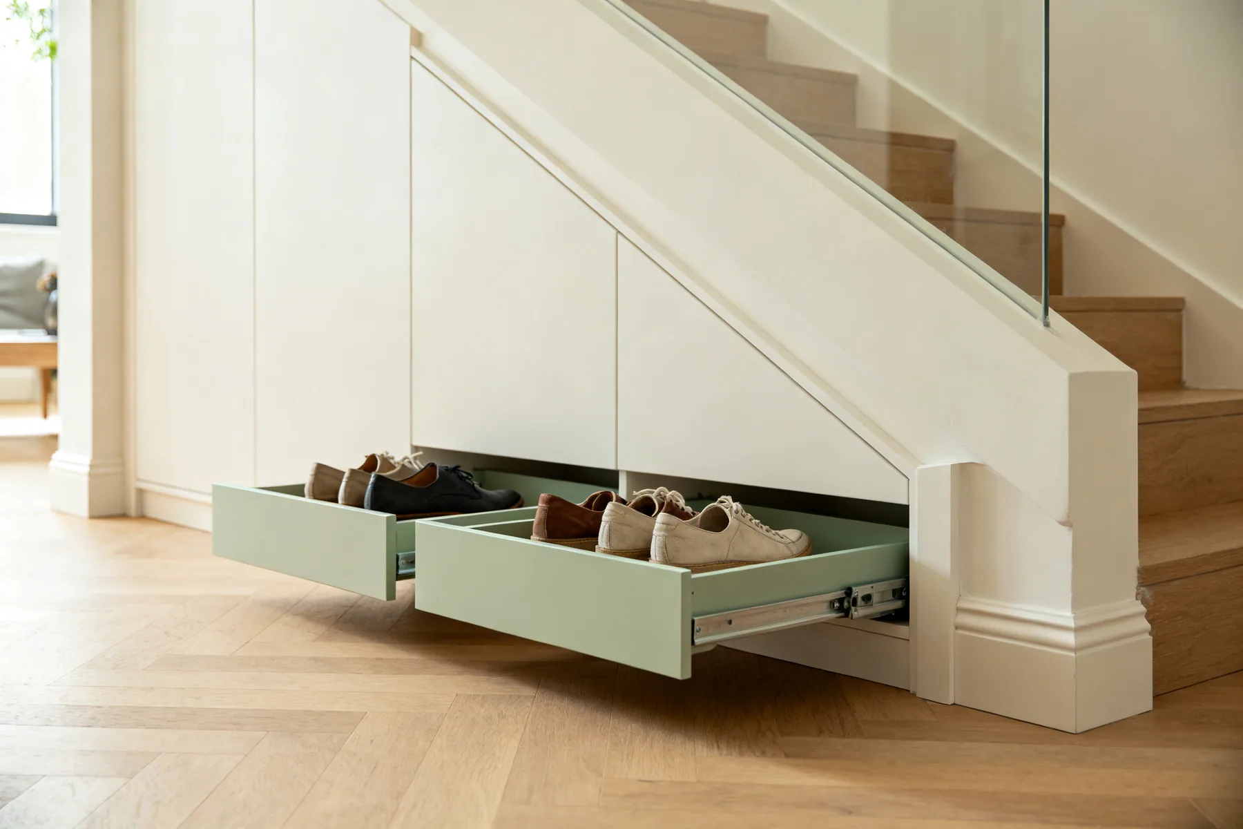 The shallowest 400mm, which only ever works as trays Two low angled slide-out trays pulled out from the shallow end of an understairs run, each holding two rows of shoes, with the low diagonal stair soffit visible above
